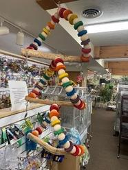 Colorful bird toy featuring a triangular design with wooden beads and a perch, displayed in a pet store. Ideal for enriching avian environments.